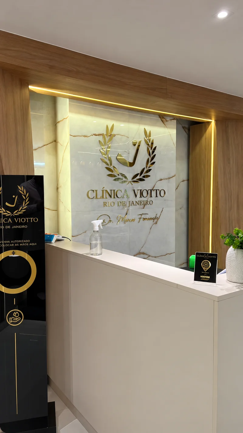 Recepção da Clínica Viotto Rio de Janeiro, com balcão branco e logotipo dourado no painel de mármore.